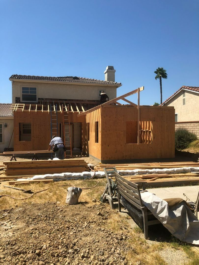 Partially built house with wooden framing and workers in a dry yard under a clear blue sky