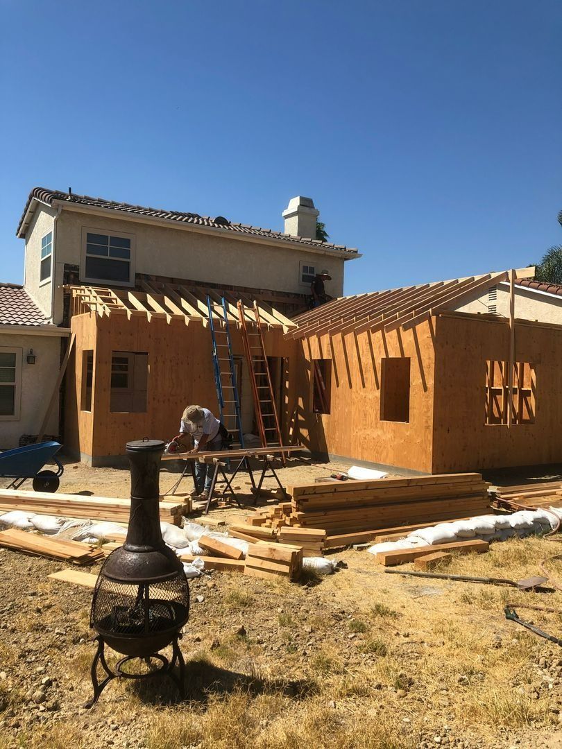 Partially built adobe-style house with ladder and chimney under a clear blue sky