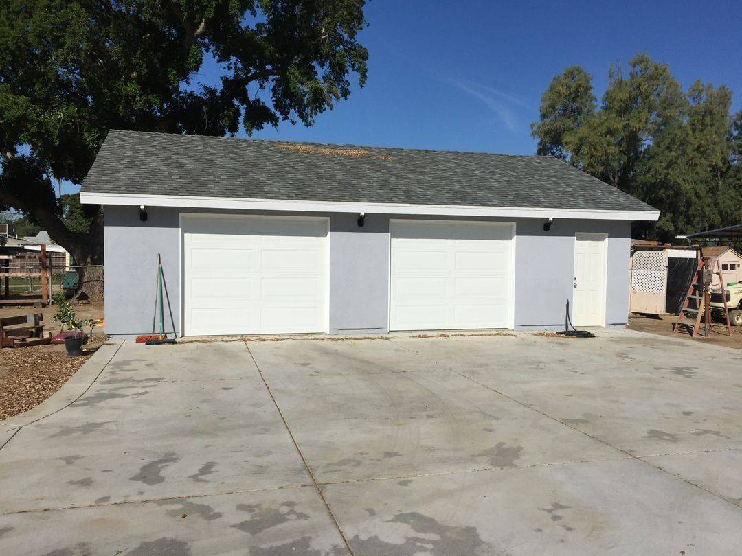 White two-bay garage with a gray roof and concrete driveway under a clear blue sky
