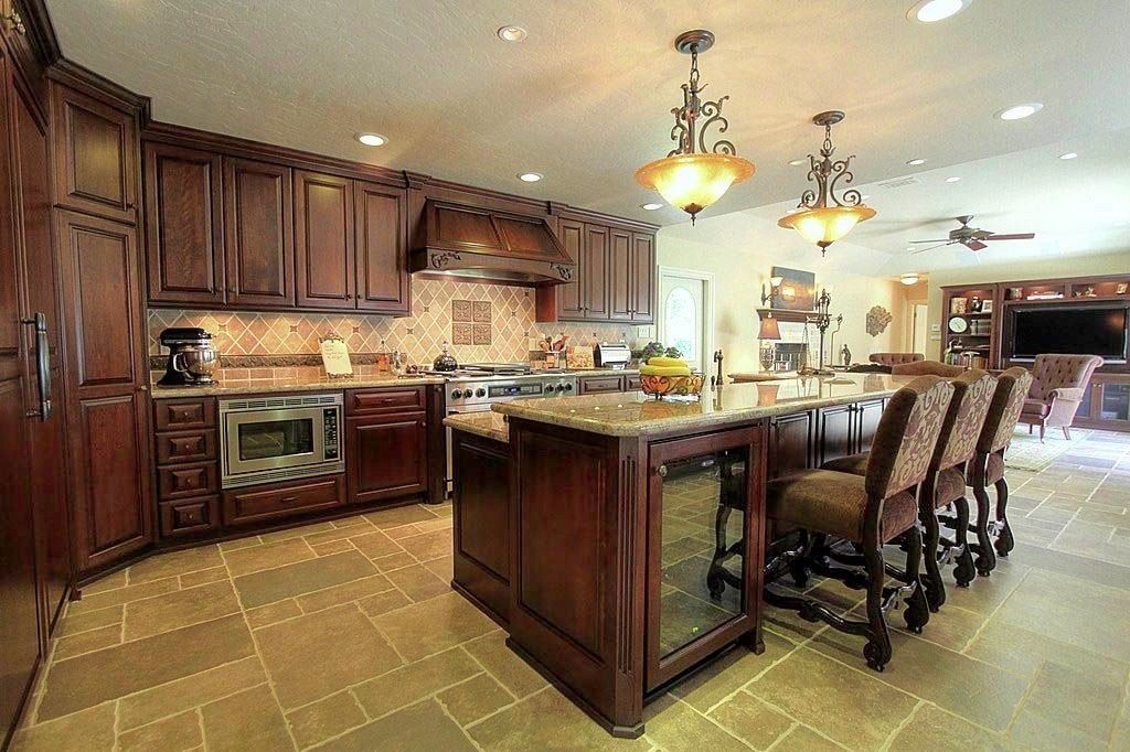 Spacious kitchen with dark wood cabinets, large island, pendant lights, and barstools on tiled floor