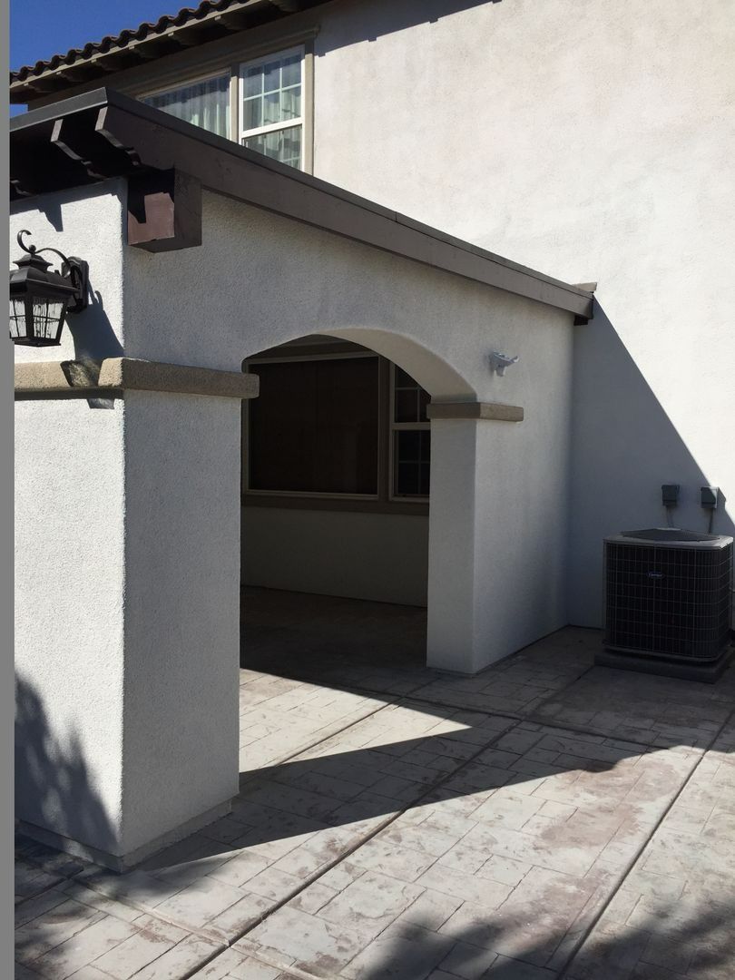 Sunlit stucco patio with arched entryway, gray columns, tiled floor, and a wall-mounted light