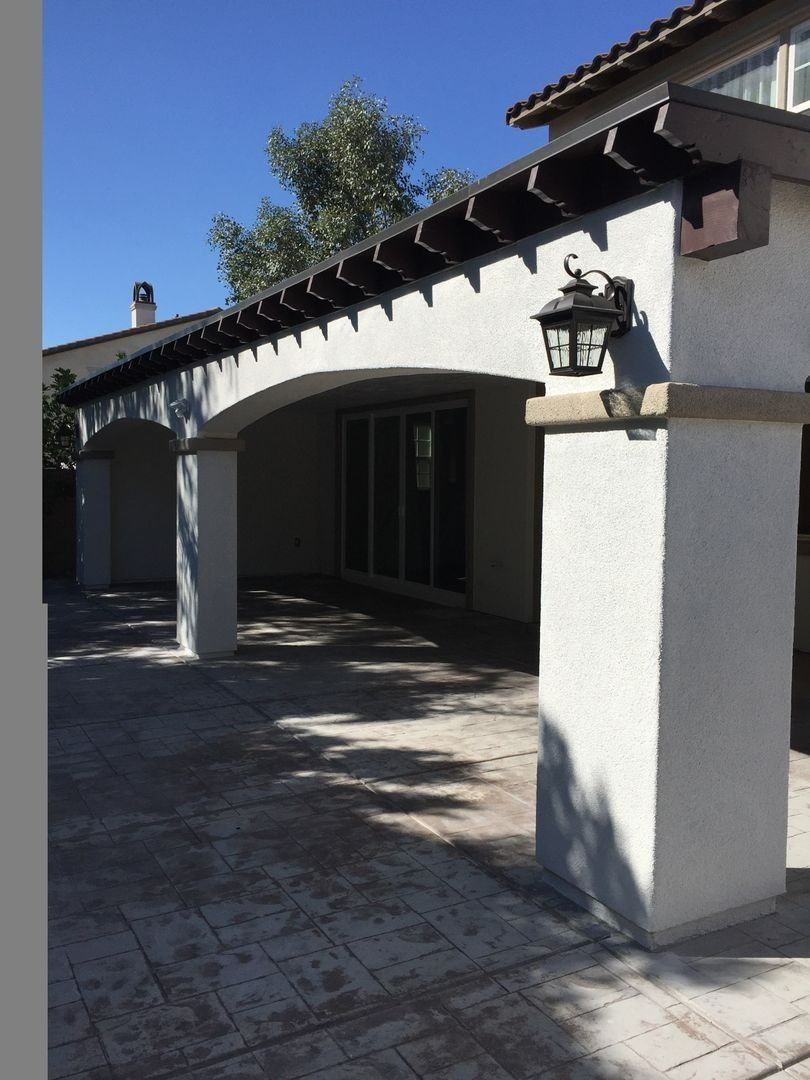 Covered courtyard entrance with white stucco columns, lanterns, and a tiled walkway in bright sunlight