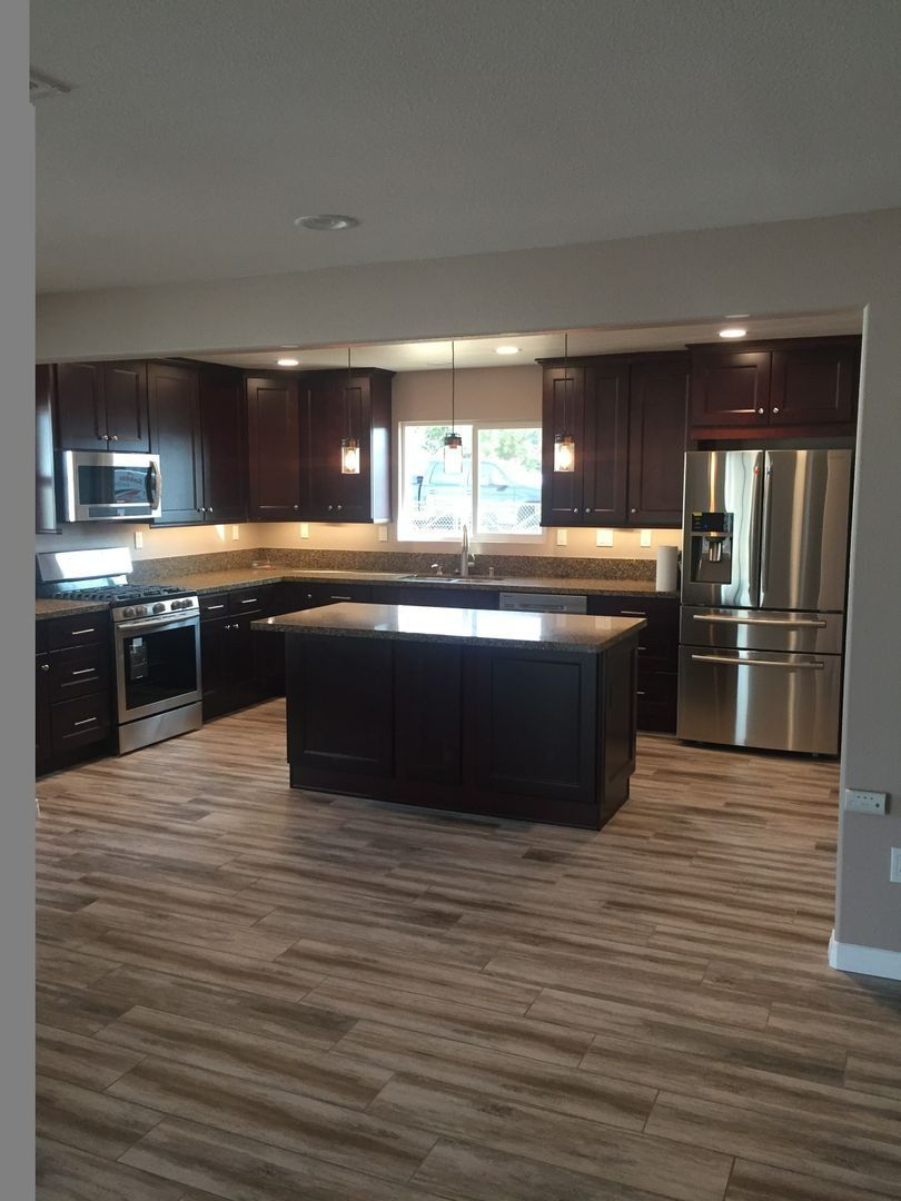 Modern kitchen with dark wood cabinets, stainless appliances, island, and wood-look flooring