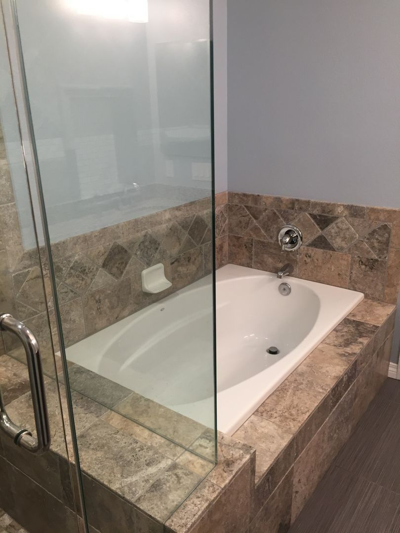 Glass-enclosed bathtub with stone tile surround in a modern bathroom
