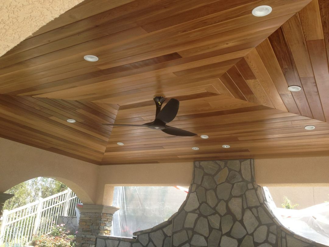 Covered patio ceiling with a dark bird flying beneath wooden beams and recessed lights