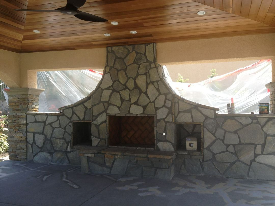 Stone fireplace under a wood ceiling in an open patio area with draped plastic sheeting.
