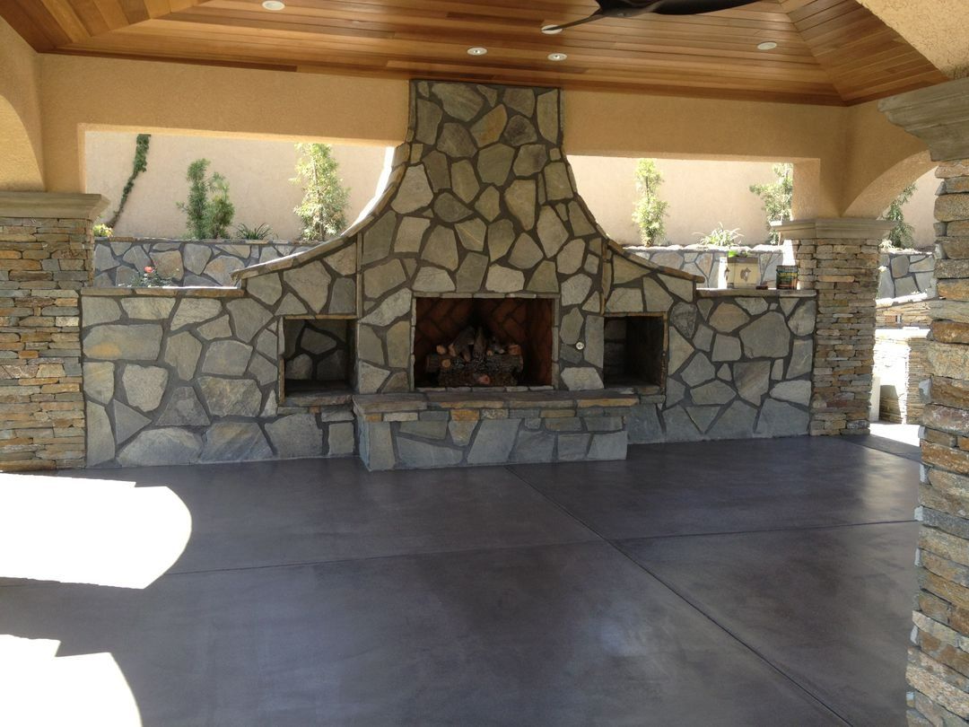 Stone outdoor fireplace under a wooden pavilion with a concrete floor