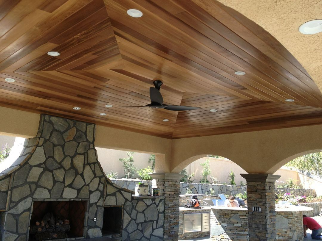 Outdoor patio with a stone fireplace, wooden ceiling, and ceiling fan under arched openings