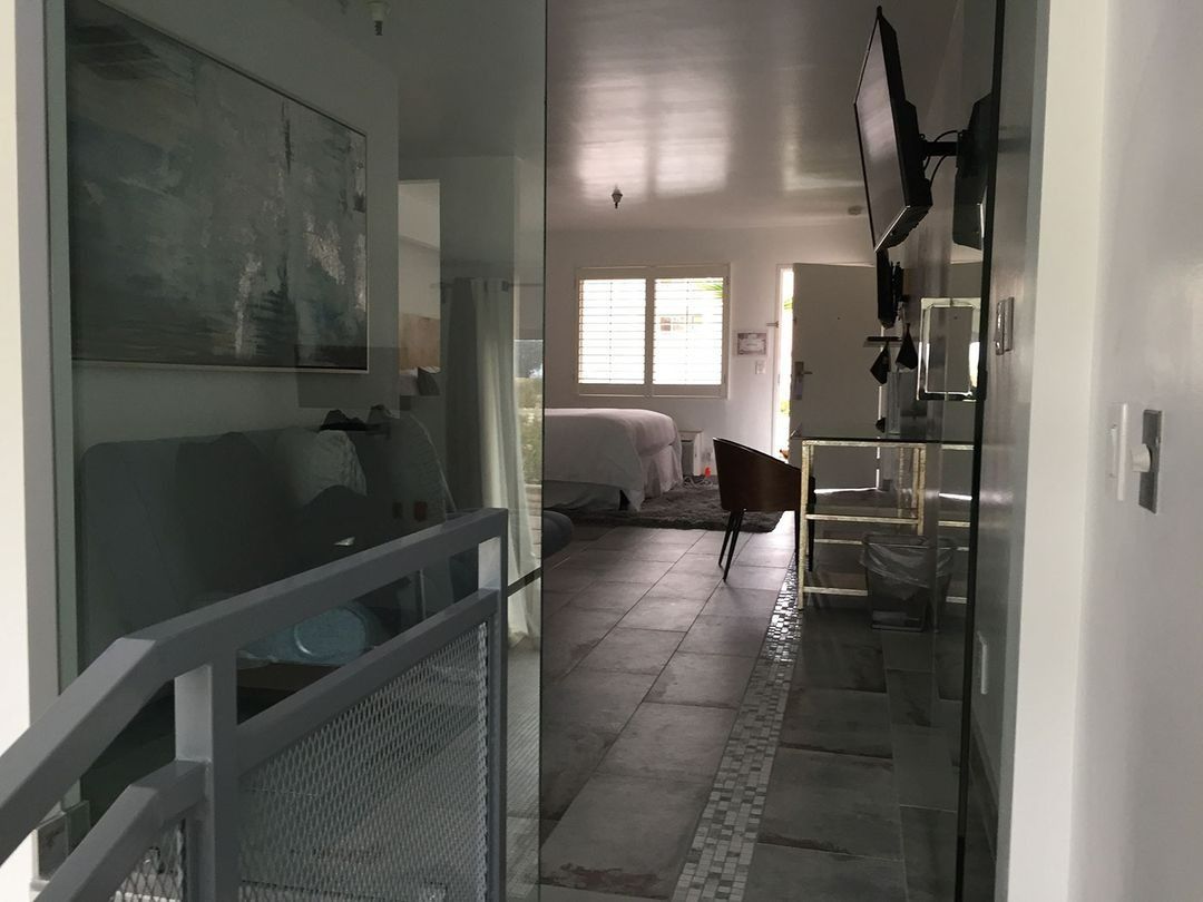 Narrow hallway with tiled floor, railing, and a small dog near a bright bedroom at the end.