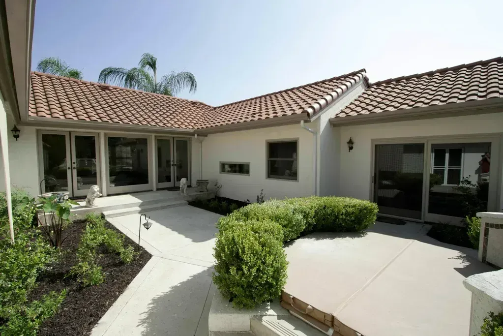 Courtyard of a modern stucco house with tile roof, white patio, and trimmed green hedges