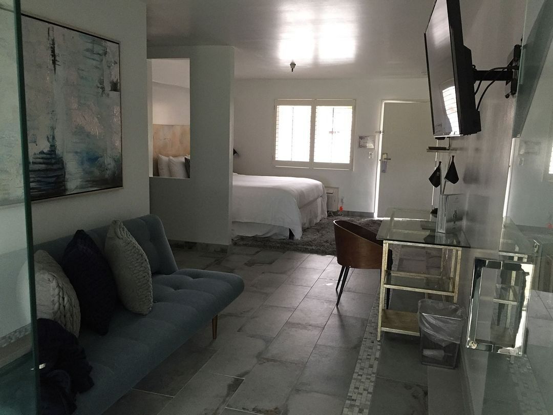 Bright white hotel room with sofa, bed, TV, and glass coffee table.