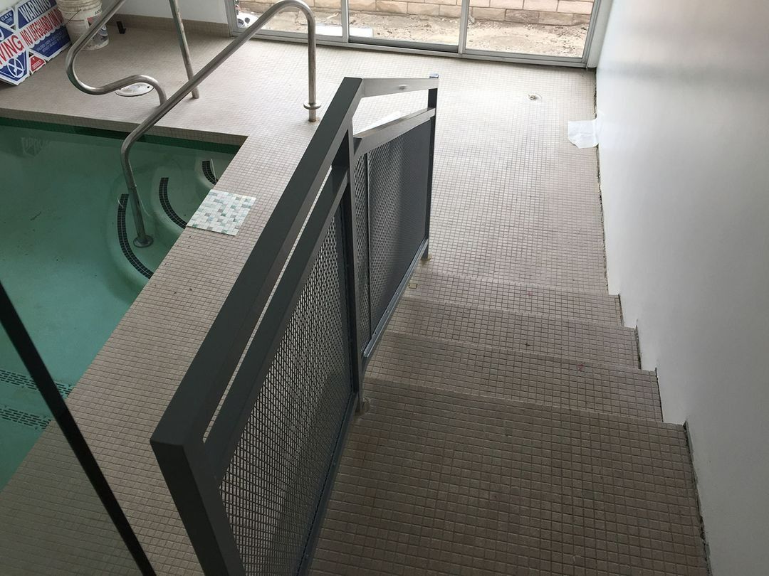 Indoor metal stairway with textured steps and black mesh railing beside a green floor area