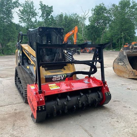 Yellow and black skid steer with rotary mower cutting brush in a field.