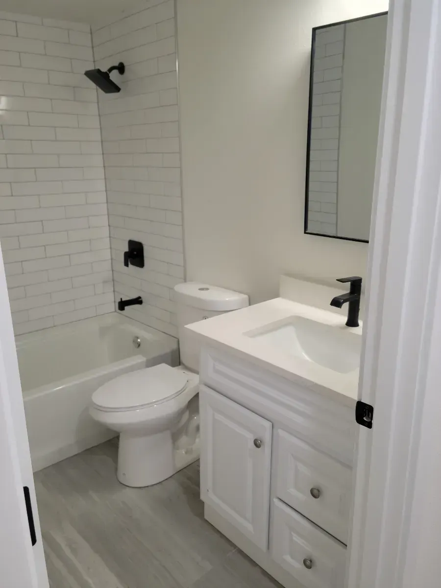 Small white bathroom with tub, toilet, sink vanity, and mirror.