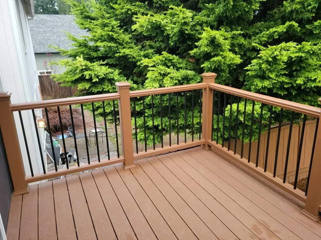 Wooden deck with brown railing and black balusters overlooking a green yard and trees