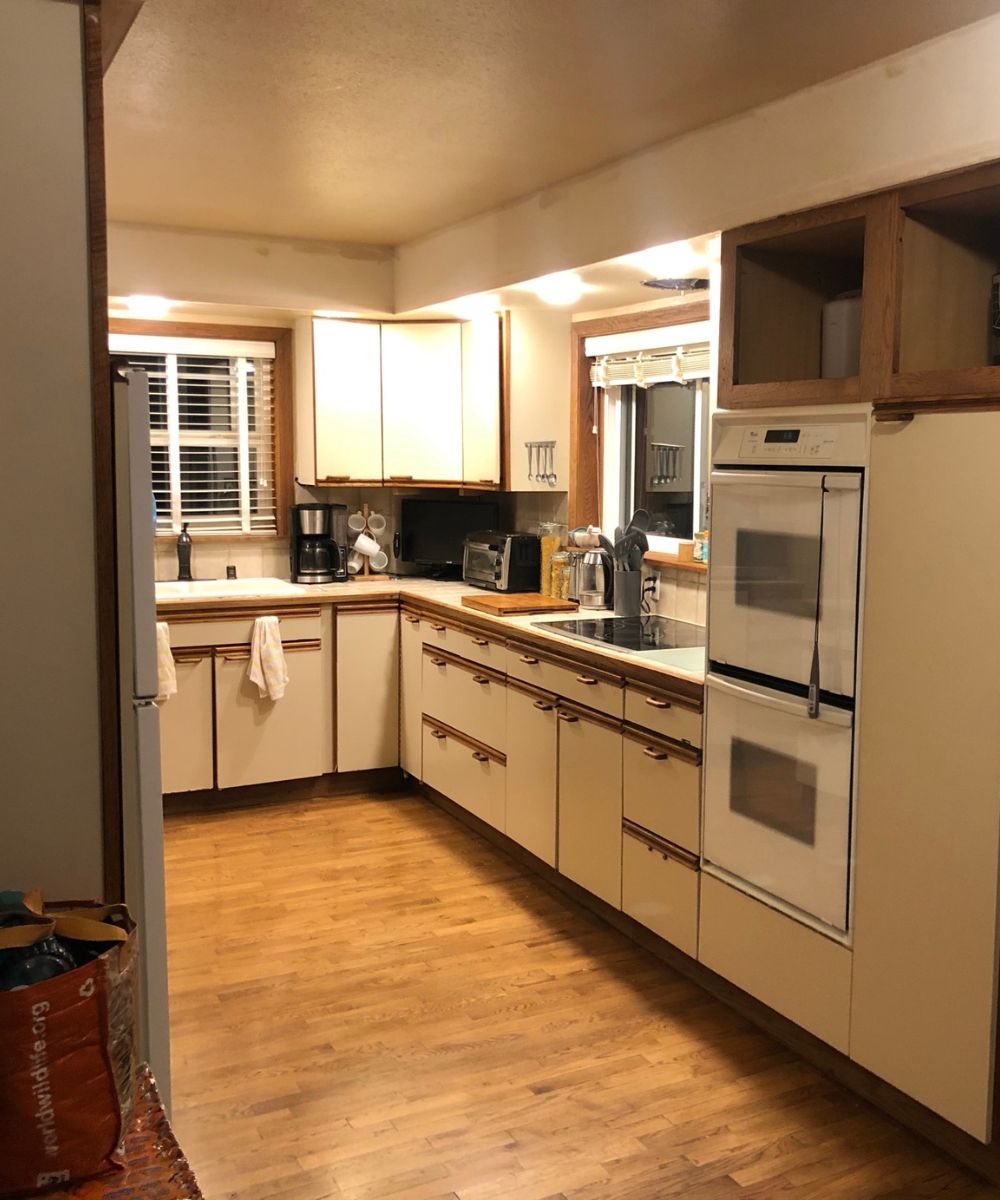 Narrow kitchen with wood floors, white cabinets, stainless appliances, and a window at the far end.
