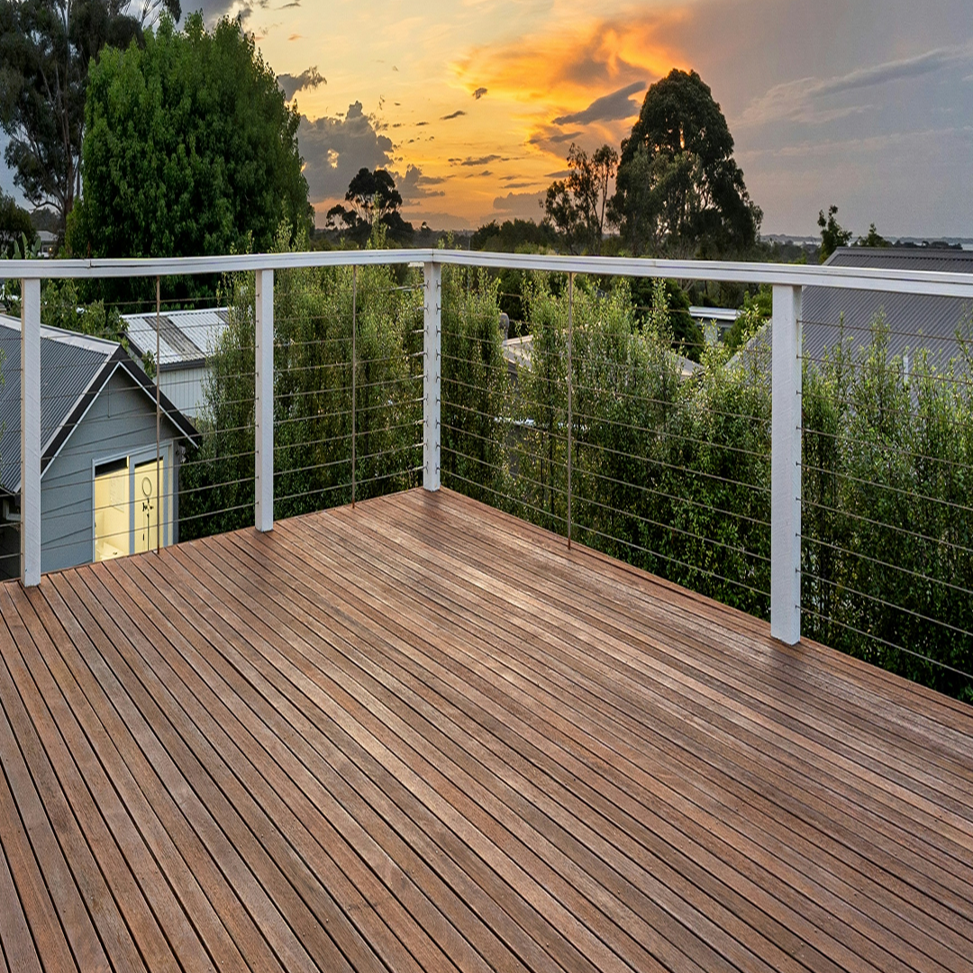 Wooden deck with white railing overlooking trees and rooftops at sunset