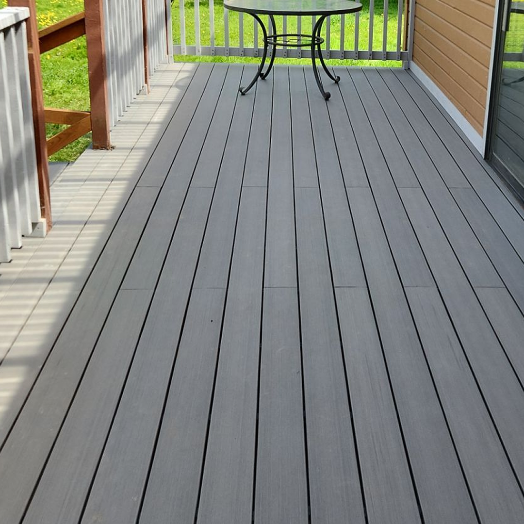 Empty gray wooden deck with railing and a small round table near the far end.