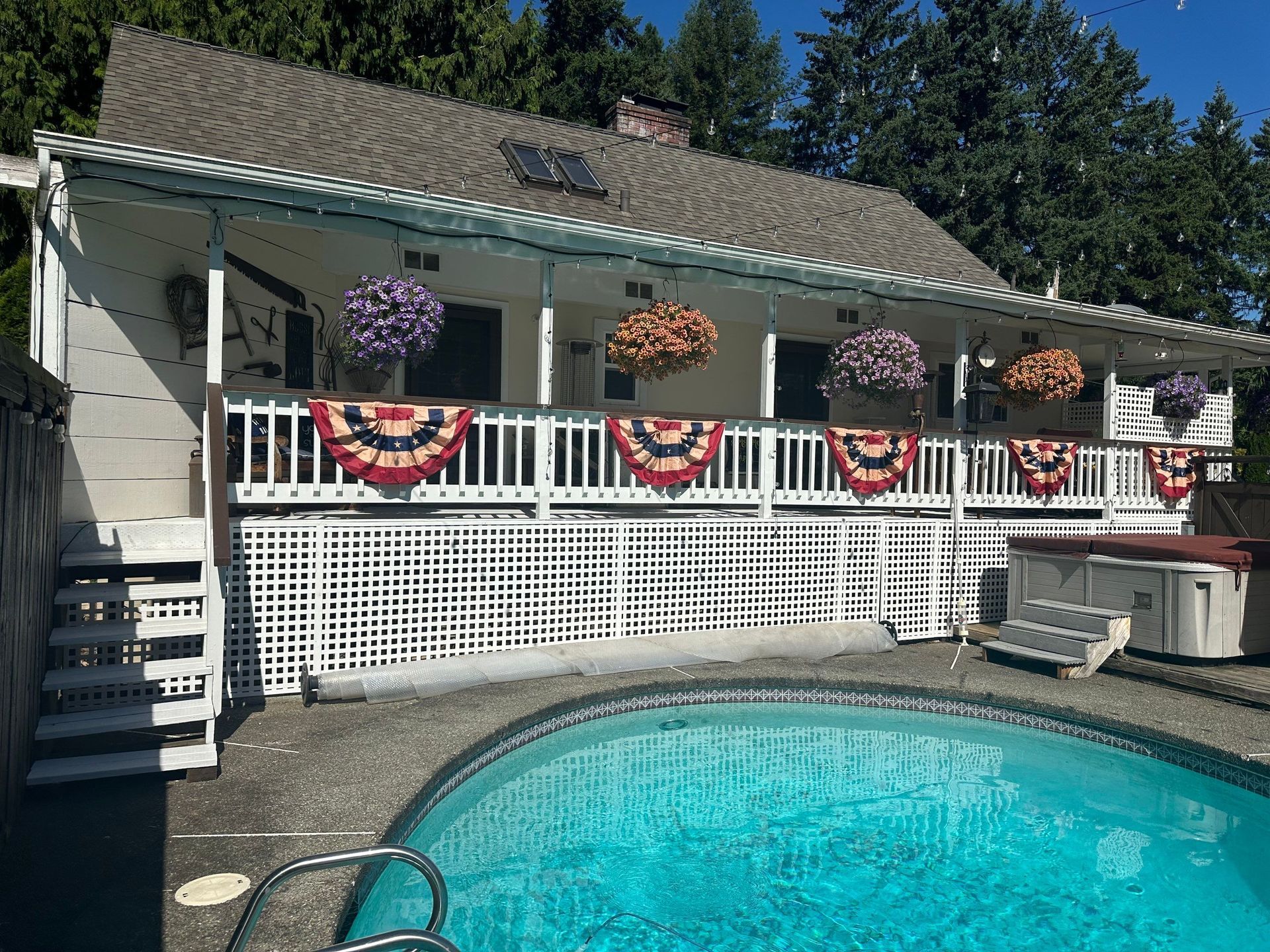 Backyard pool with a house porch decorated in red, white, and blue bunting and hanging flower baskets