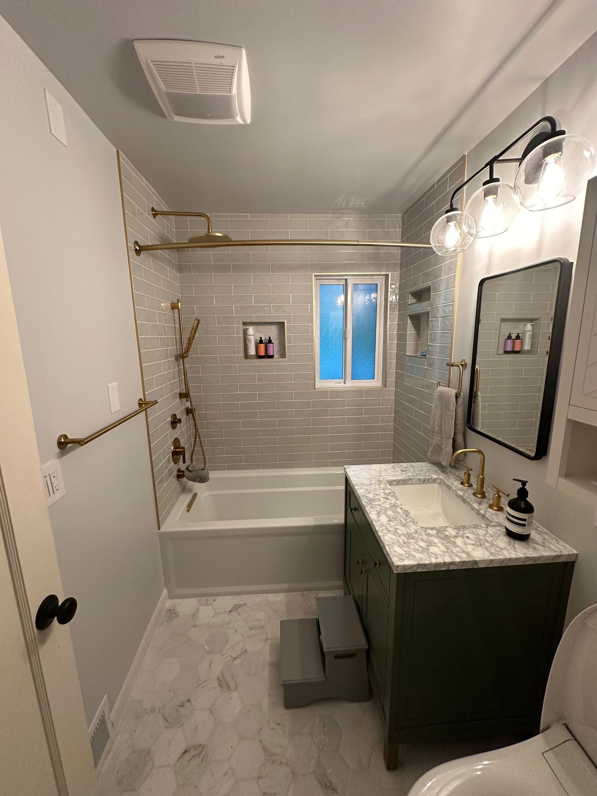Small bathroom with bathtub, green vanity, mirrored cabinet, and tiled walls.
