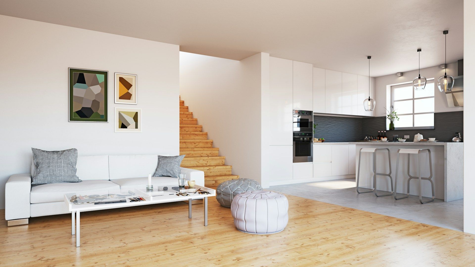 Bright minimalist living room with white sofa, wood floors, staircase, and open kitchen with bar stools.