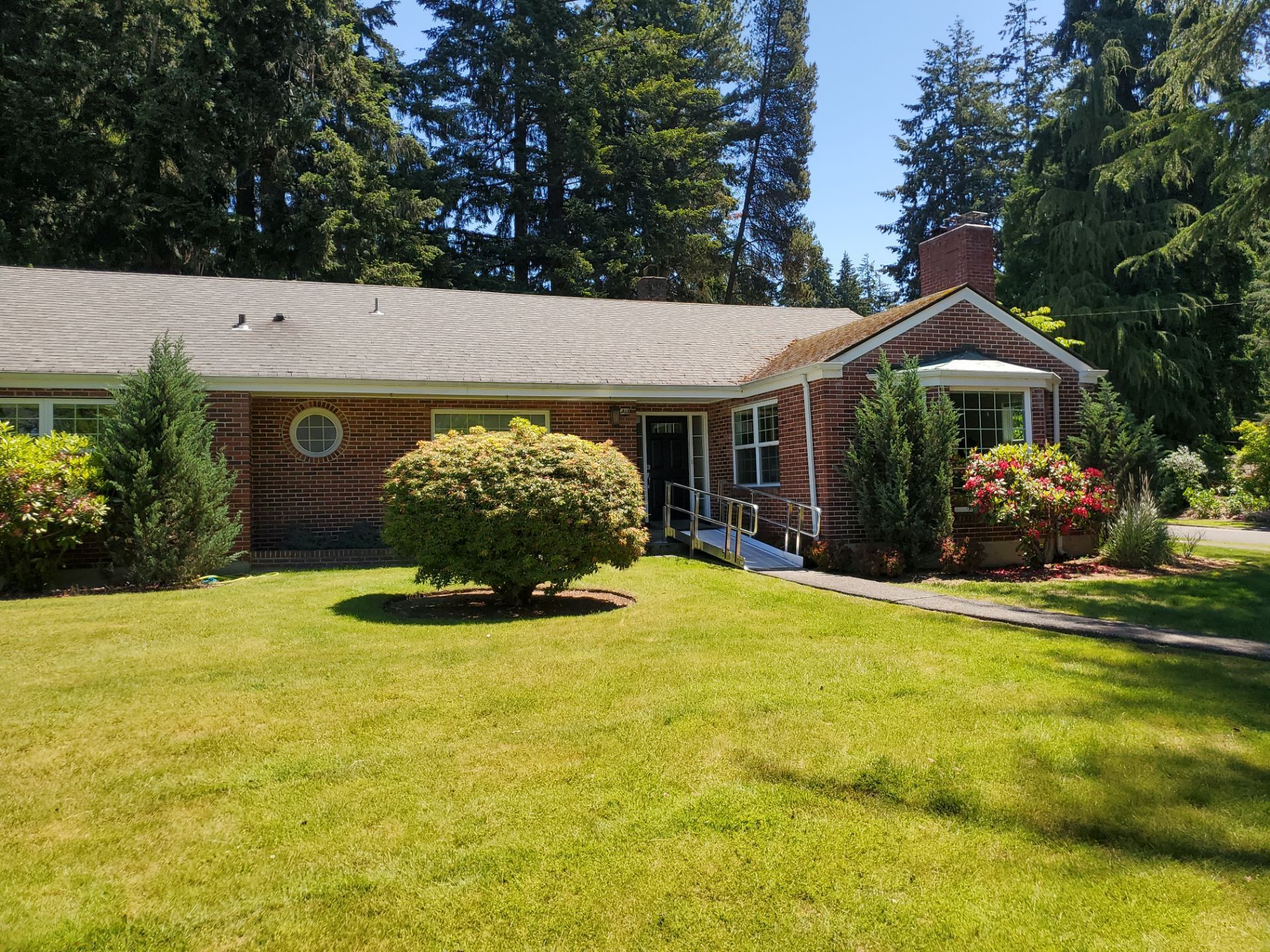 Gray house exterior with white-trimmed windows and shrubs along a green lawn
