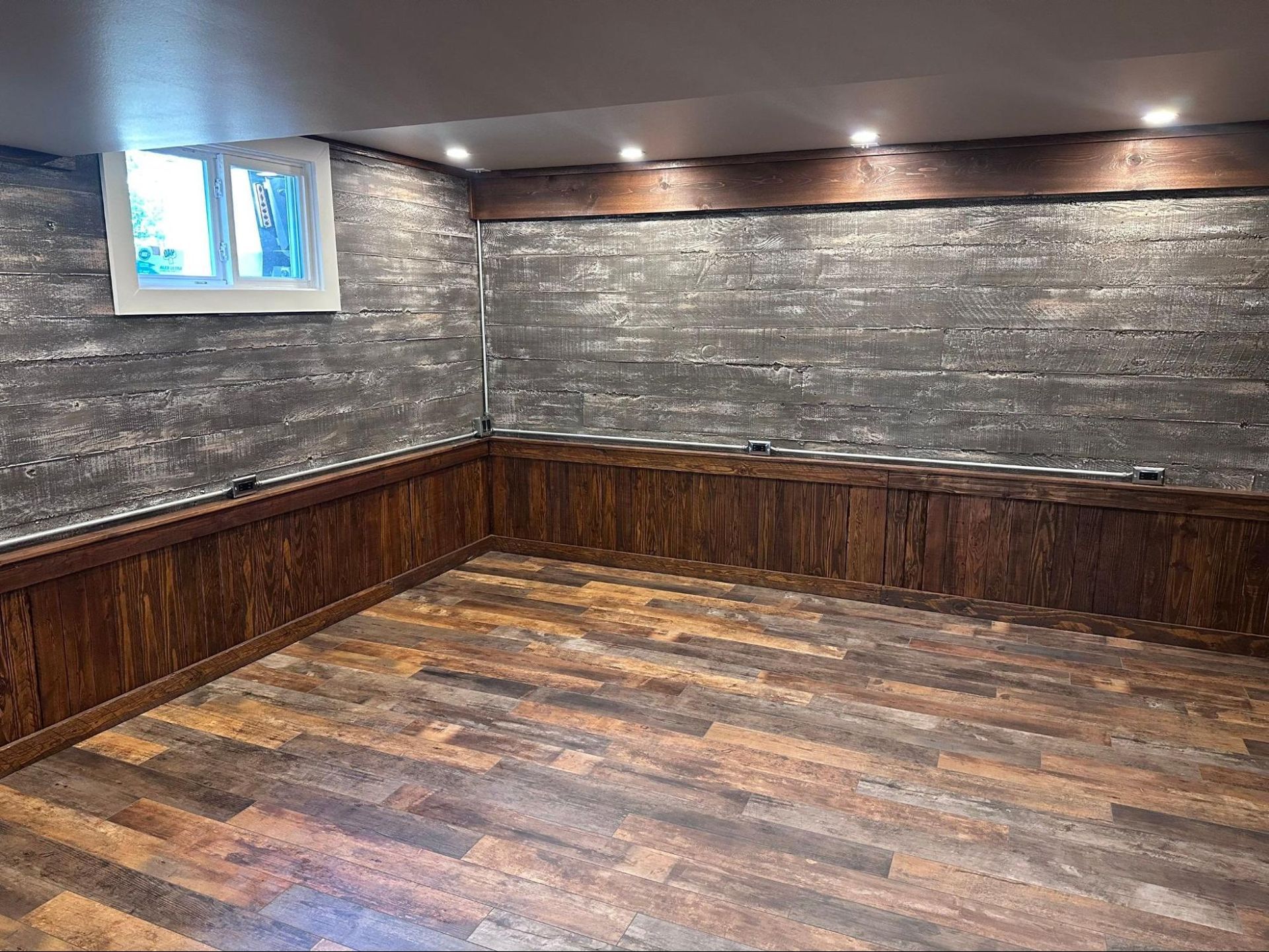 Empty basement room with wood floor, gray textured walls, and a small window