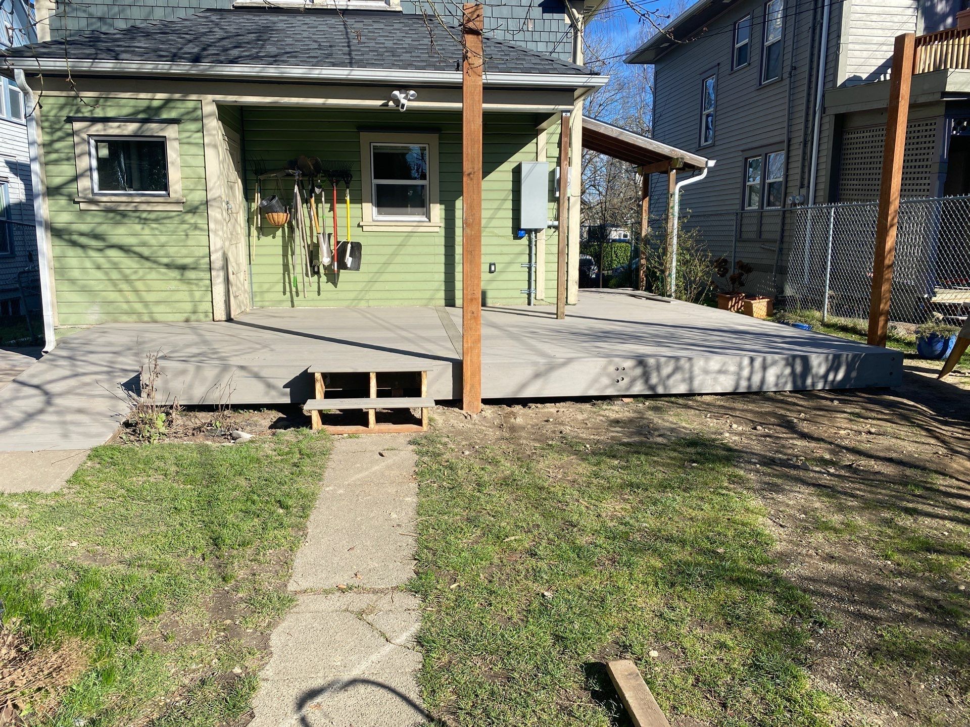 Small green house with a front porch and steps leading to a grassy yard under a blue sky.