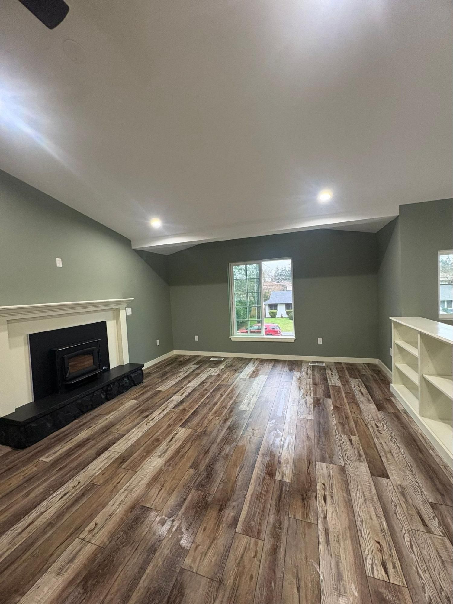 Empty living room with gray walls, wood-look floor, fireplace, window, and built-in shelves.