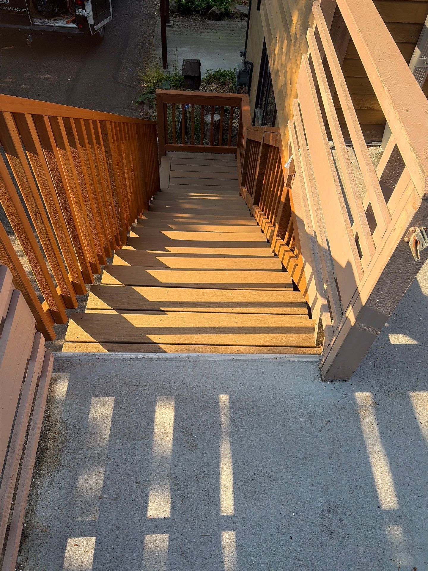 Sunlit wooden staircase with railings leading down to a patio or yard.