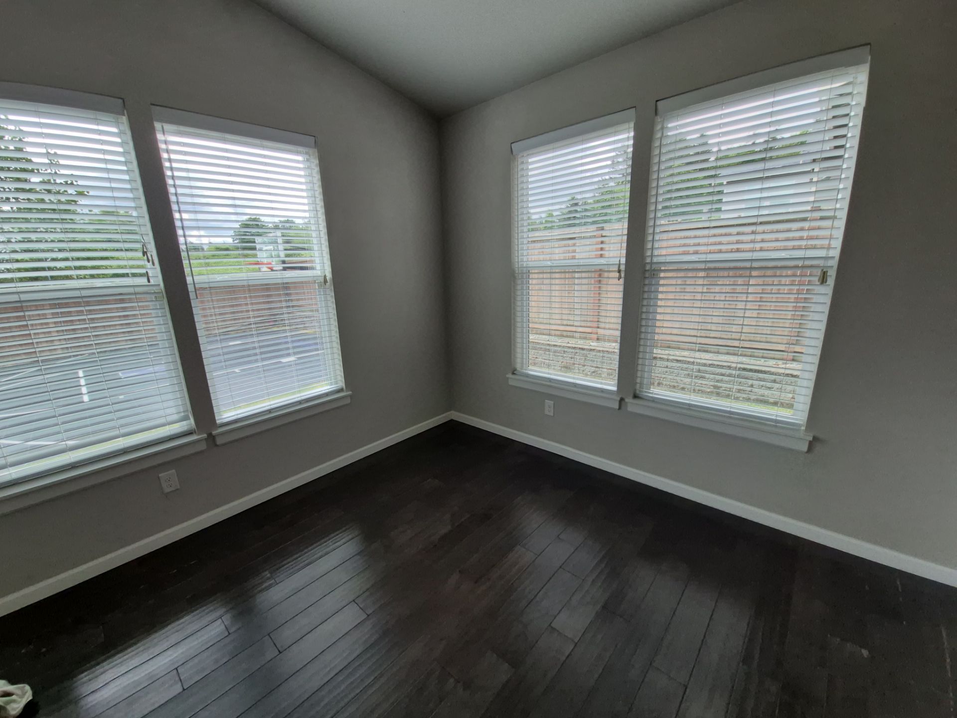 Empty room with dark hardwood floors and large windows with white blinds