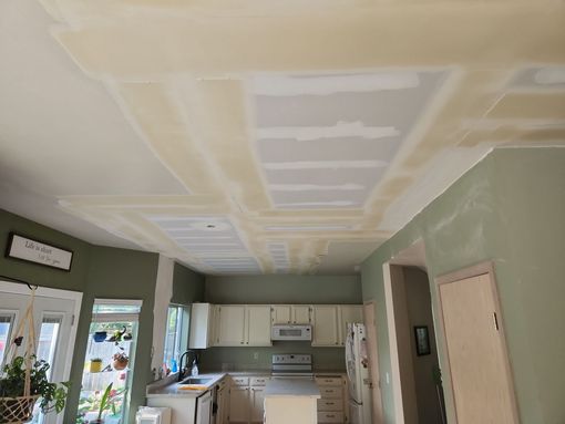 Kitchen under renovation with taped drywall ceiling, white cabinets, and green walls