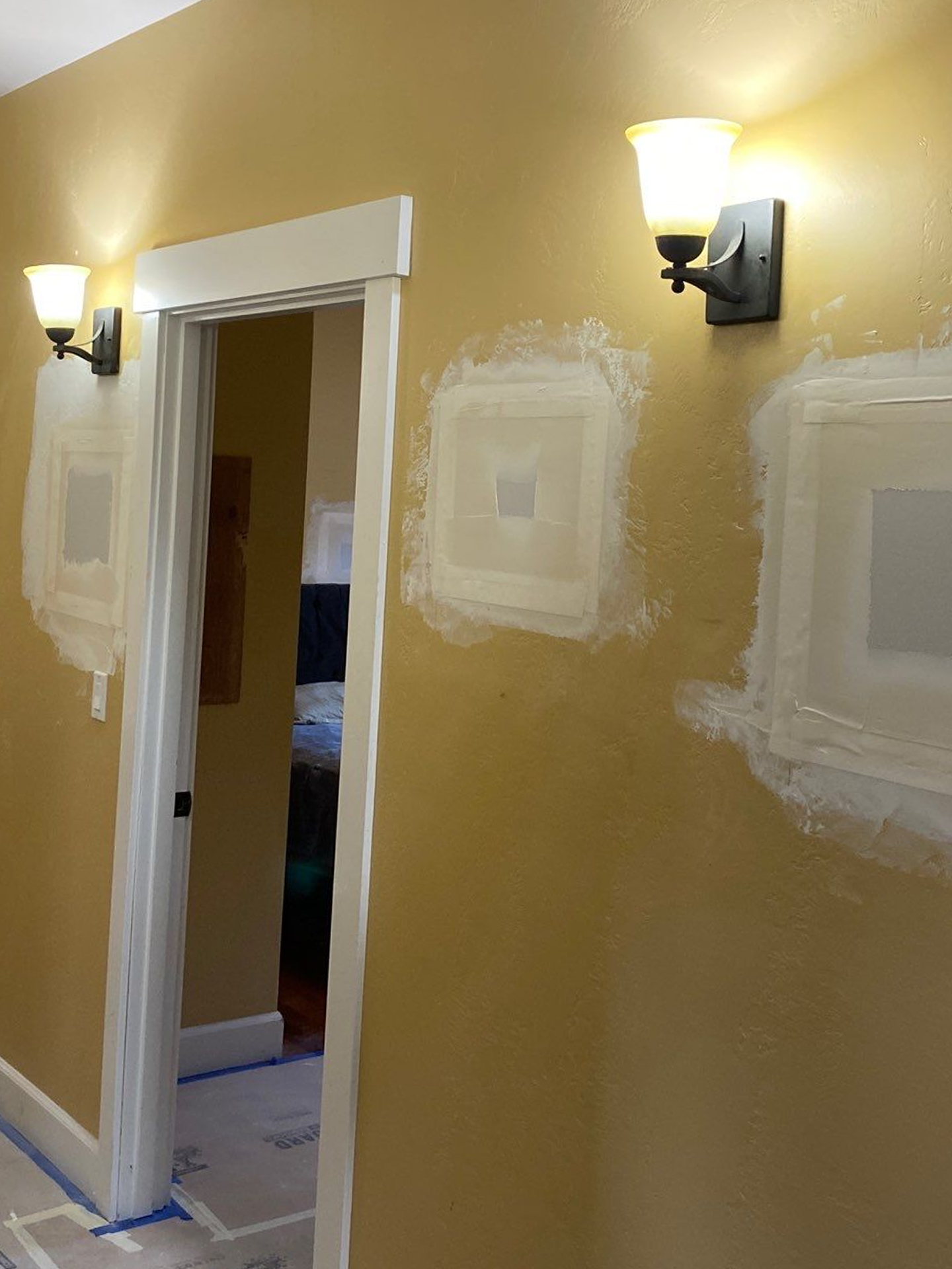 Hallway with yellow walls, wall sconces, and fresh white paint patches around a doorway
