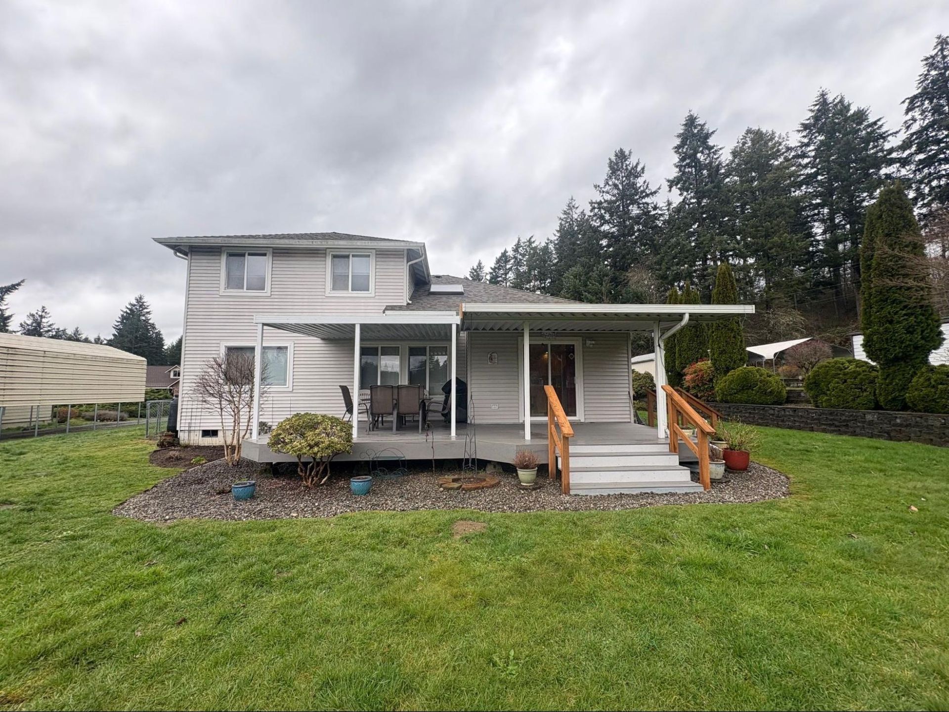 Two-story house with a covered porch, steps, and a large green lawn under cloudy skies
