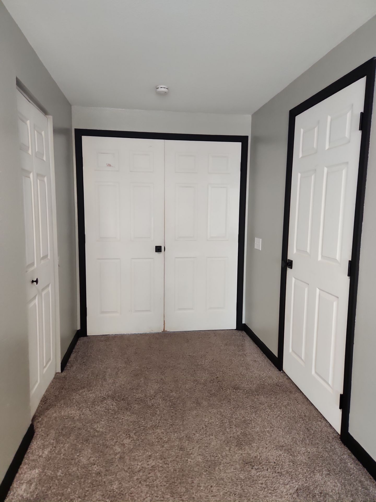Narrow carpeted hallway with white doors, gray walls, and black trim on both sides.