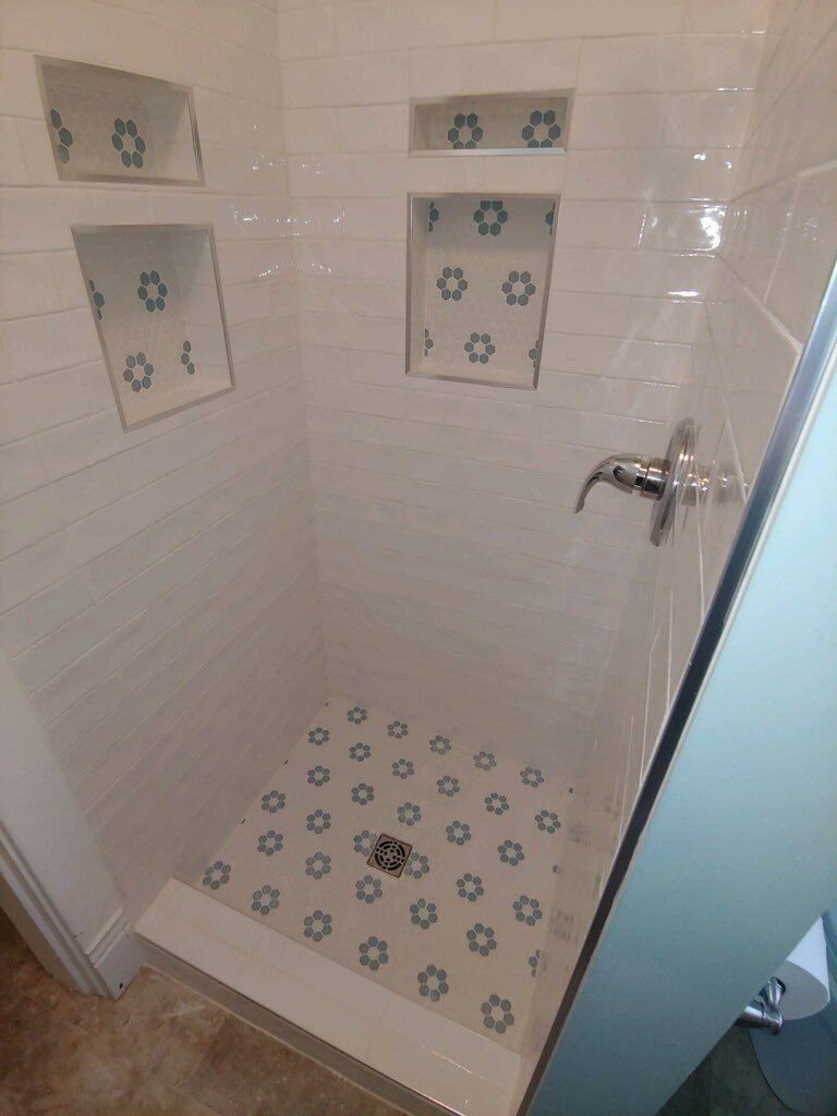 Small tiled shower stall with blue floral tile accents and a chrome showerhead.