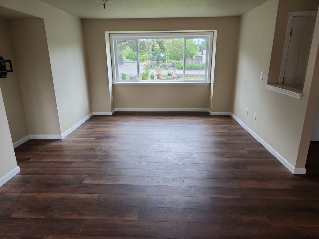 Empty living room with wood floors and a large window letting in natural light.