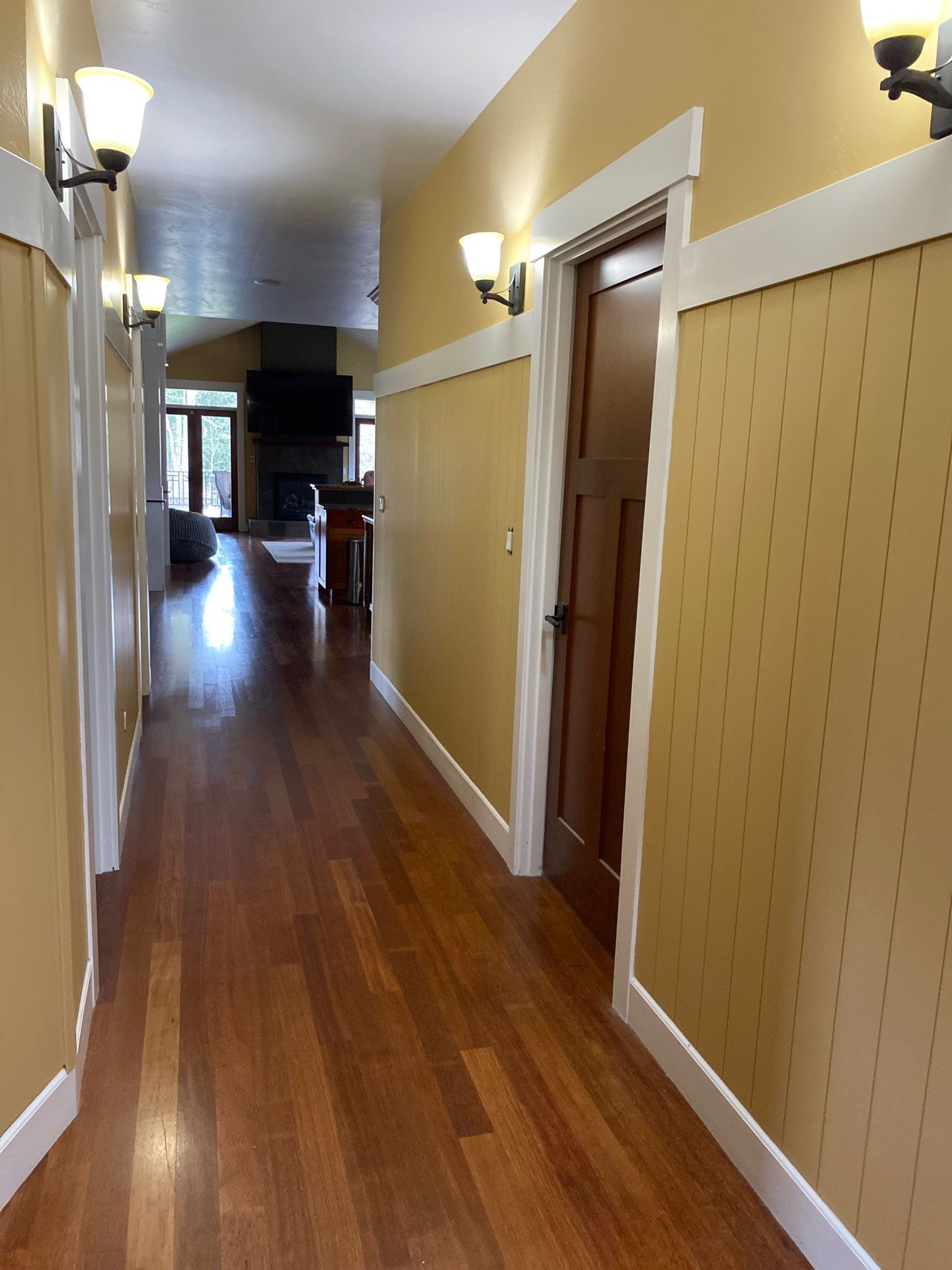 Narrow hallway with wood floor, cream walls, wall sconces, and an open doorway on the right.