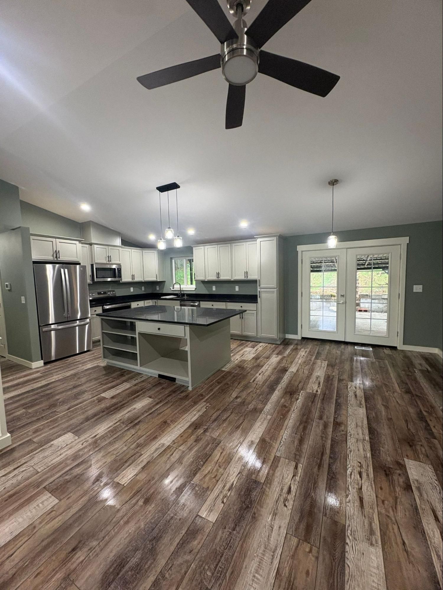 Spacious modern kitchen with stainless appliances, island, wood floors, and French doors to outside.