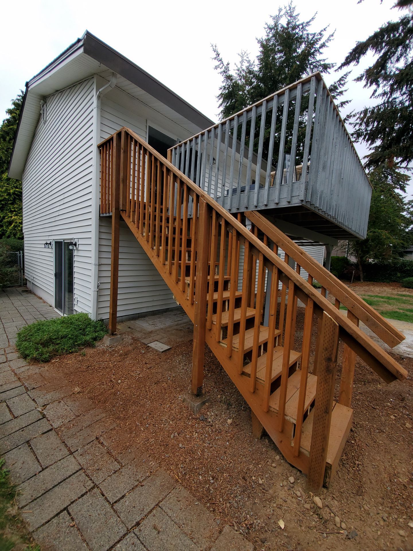 Exterior stairway leading to a raised deck beside a white brick house, with wooden and metal railings.