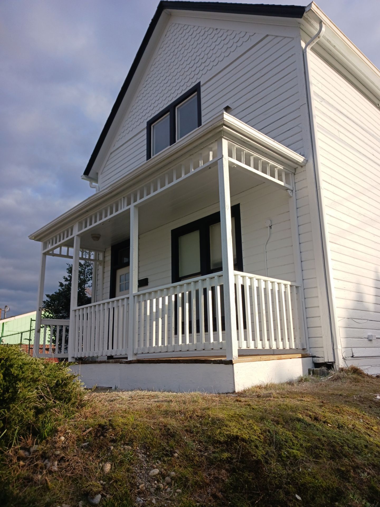 White two-story house with a front porch and railing on a sloped yard