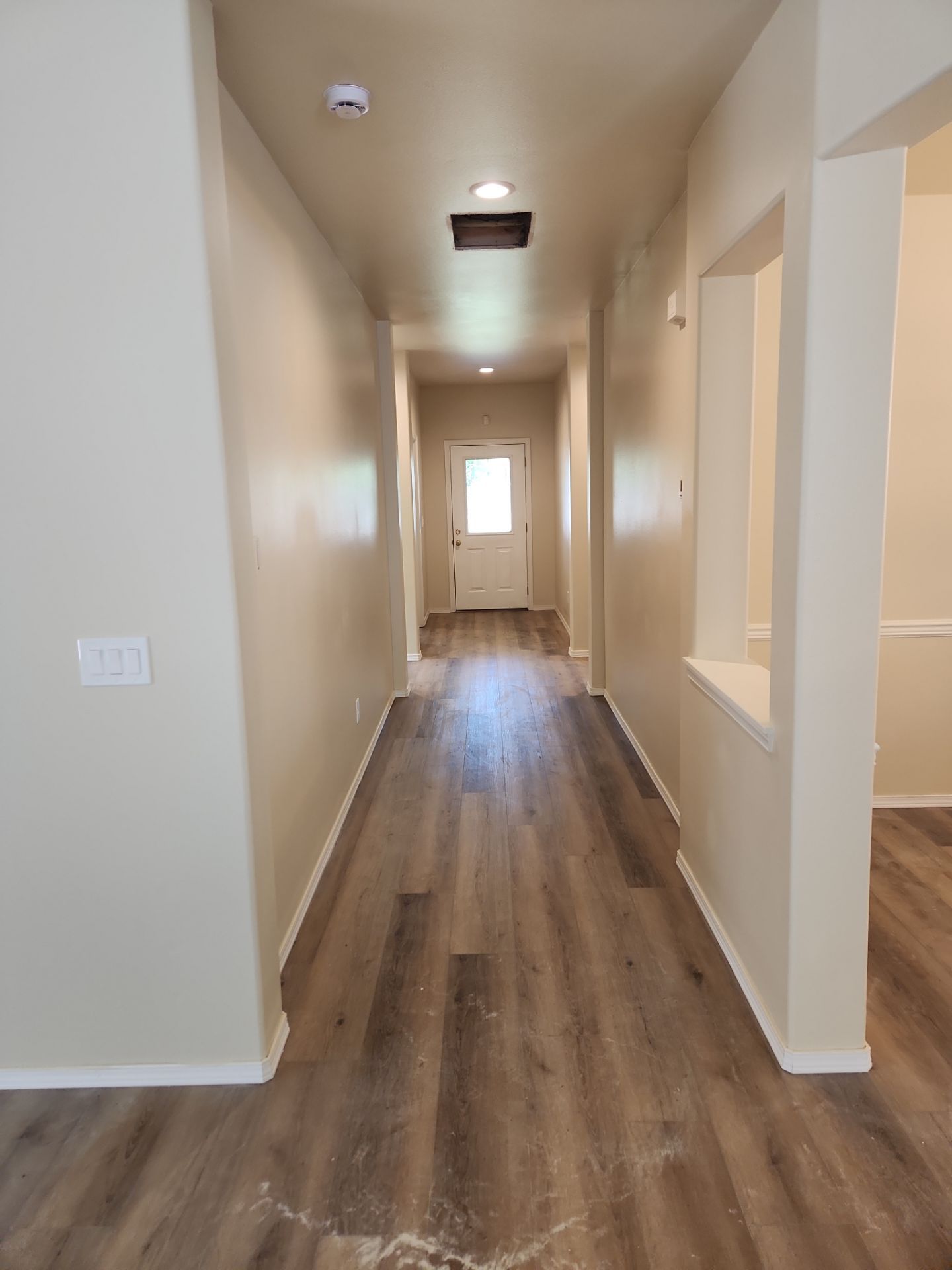 Long beige hallway with wood flooring and a door at the far end