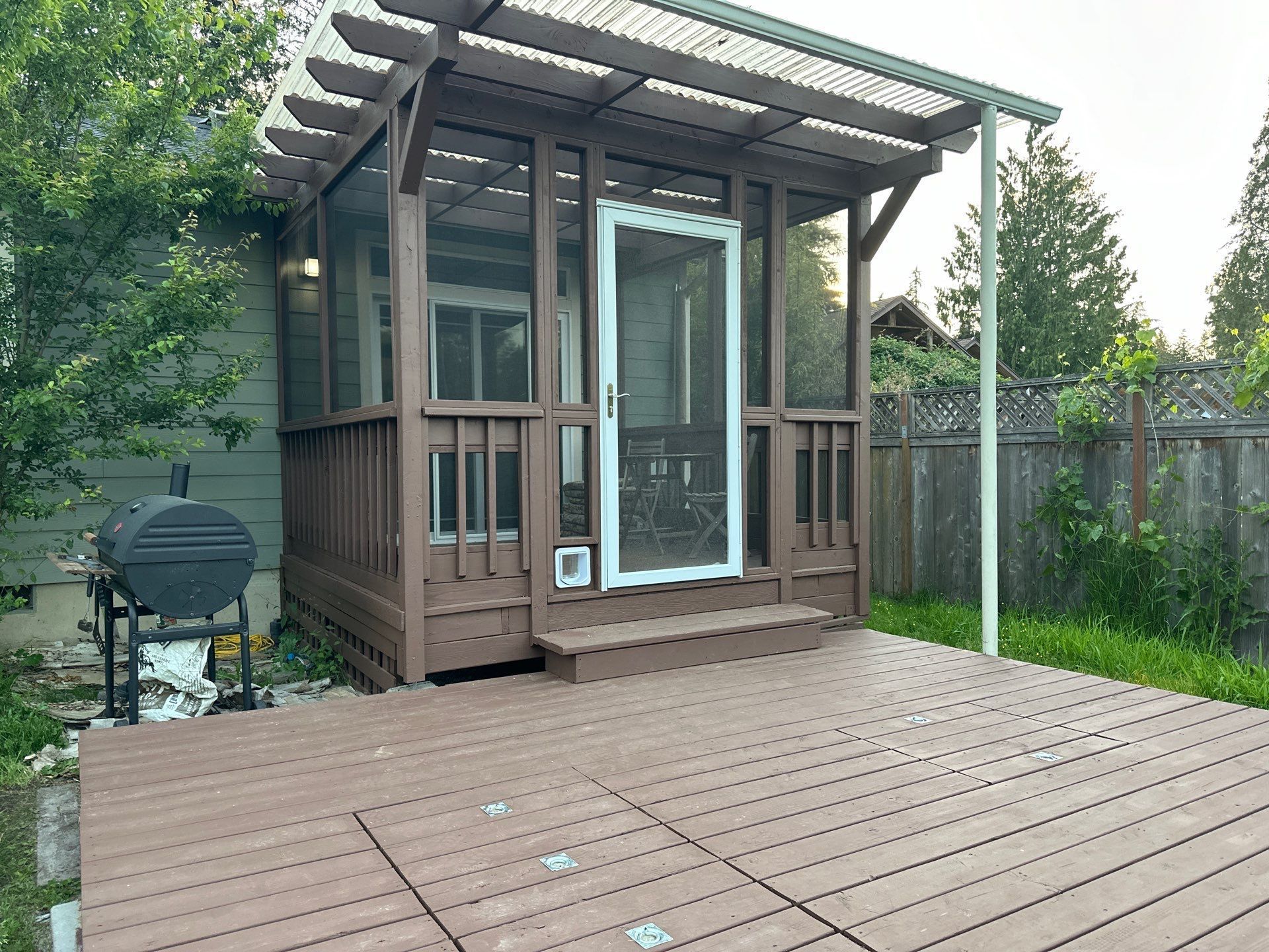 Small wooden backyard shed with a screened porch and deck in a fenced yard