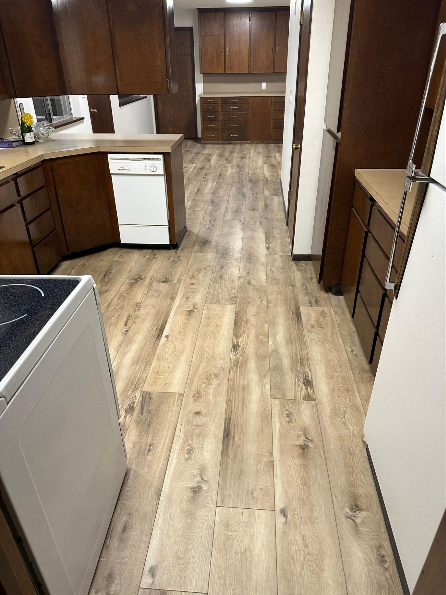 Empty kitchen with wood cabinets, white appliances, and light wood flooring.