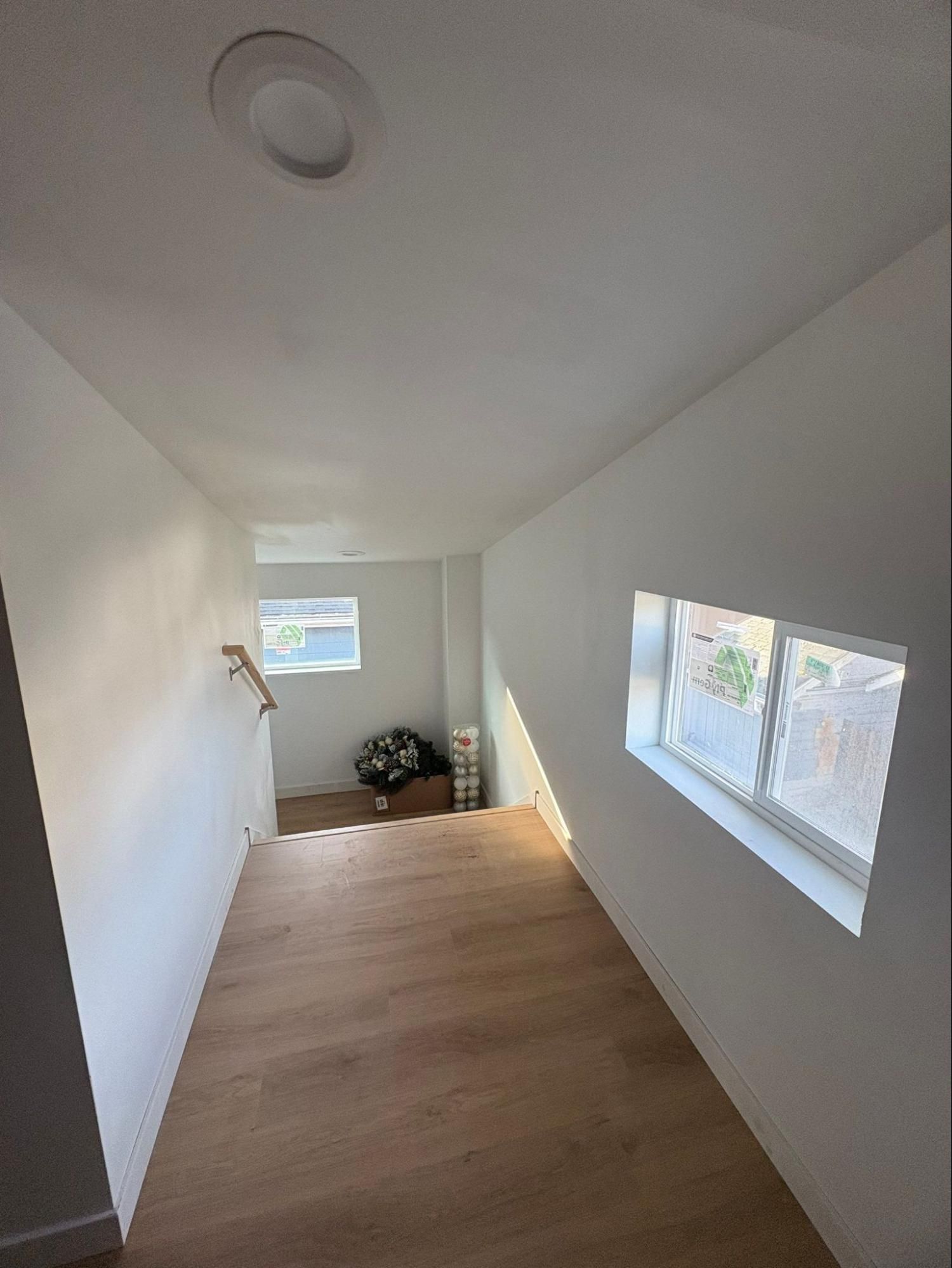 Narrow white room with wood floor, small window, and daylight streaming in through side windows.
