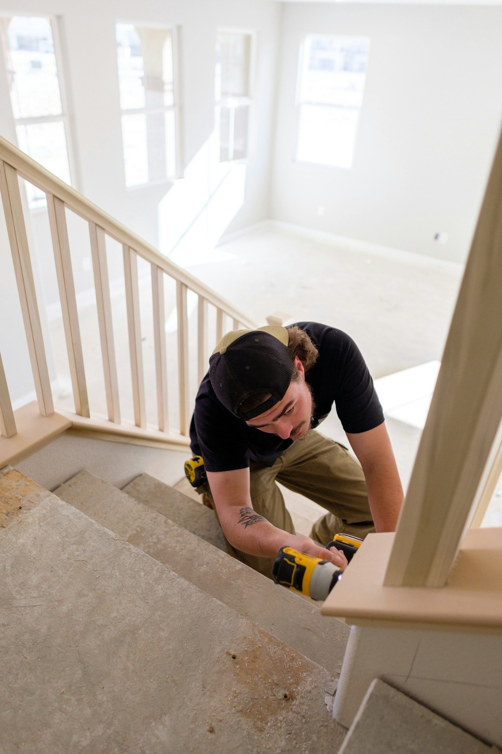 Worker kneeling on a staircase, using a yellow tool to install or repair a white railing.
