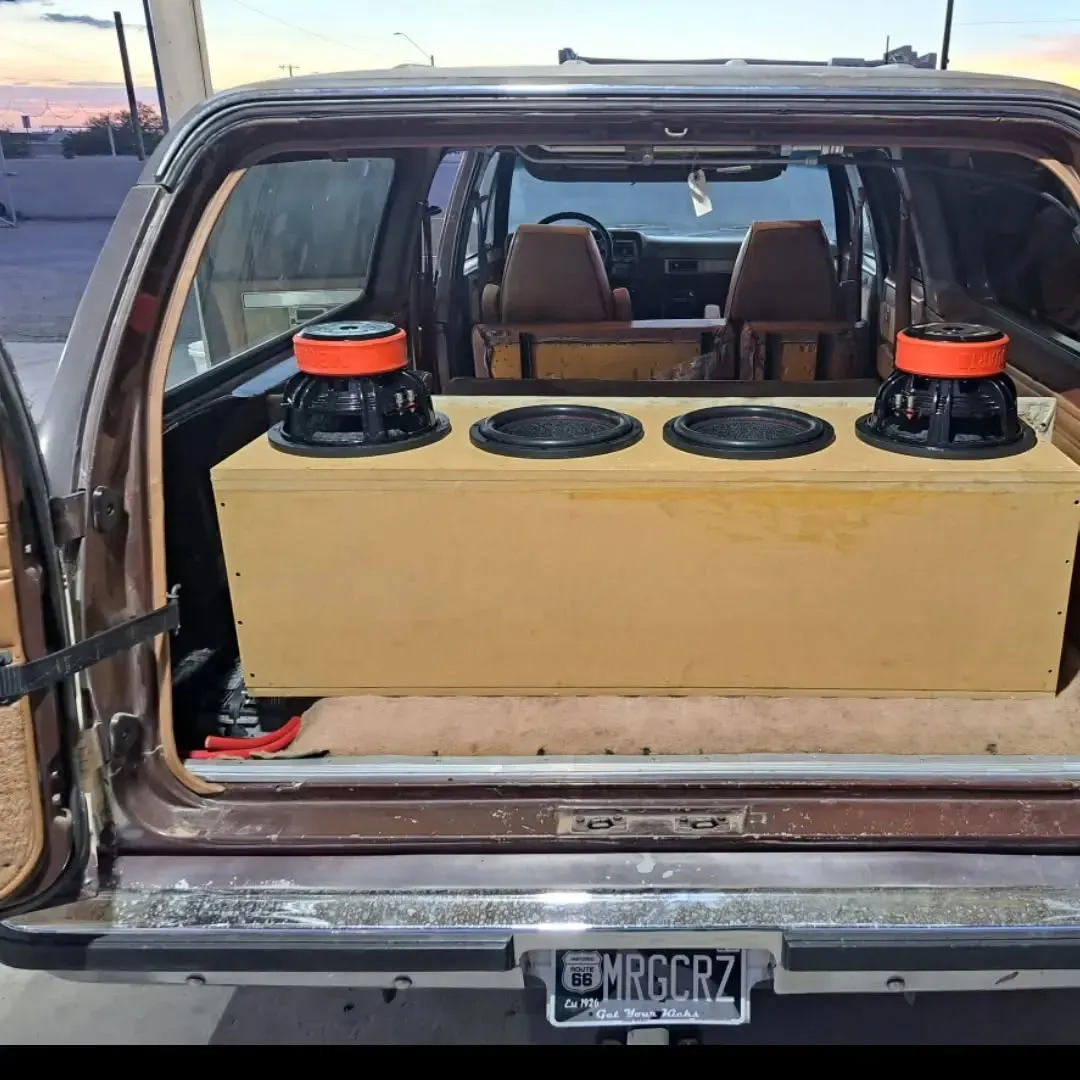 Back of a brown SUV with an open hatch, revealing a custom speaker box with three subwoofers and two speakers on top.