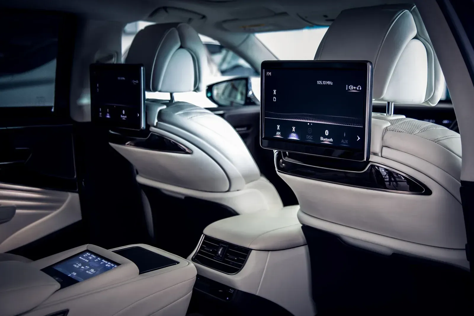 Rear interior of a luxury car with white leather seats and two screens attached 