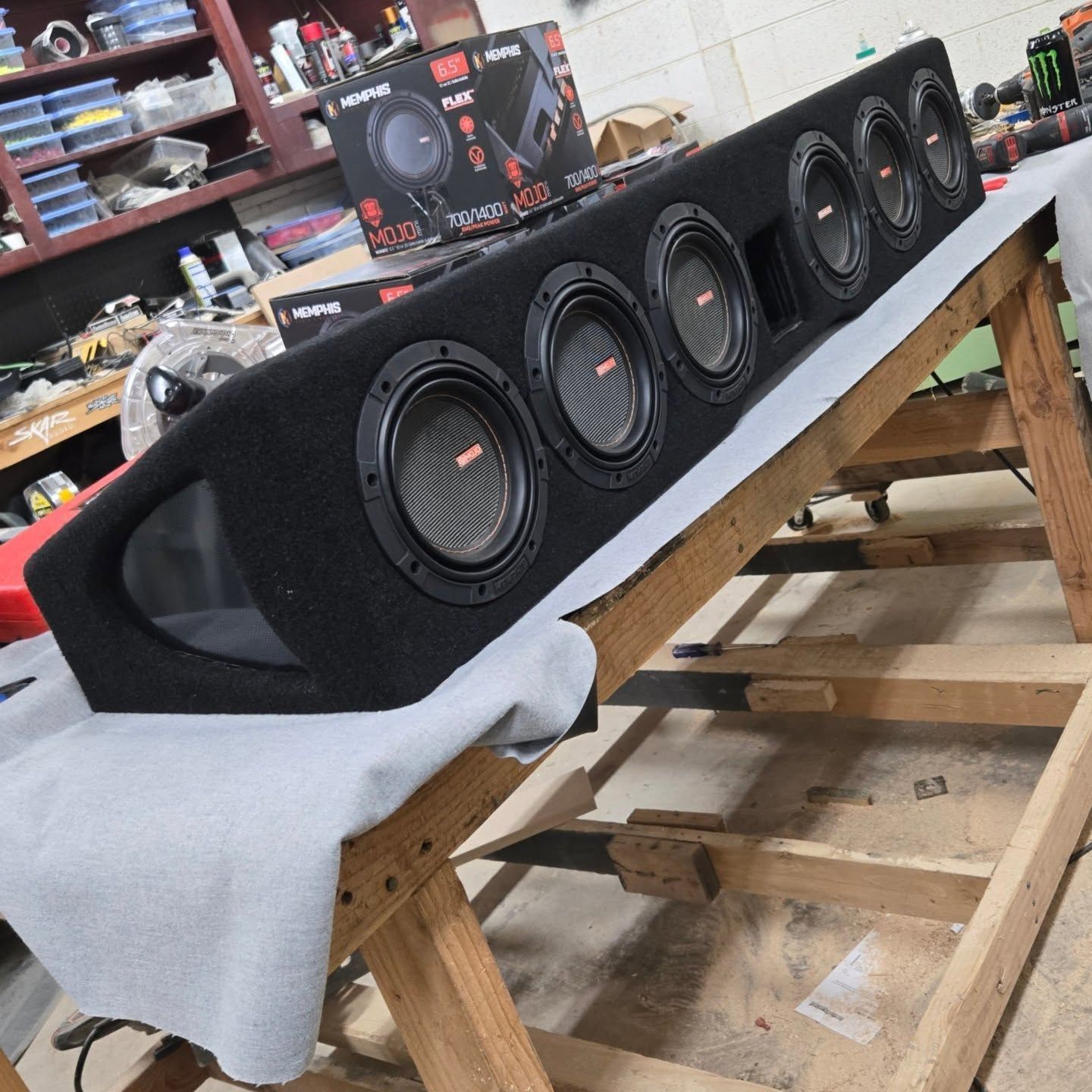 A large black speaker box with several speakers resting on a wooden support structure. Shop in background.