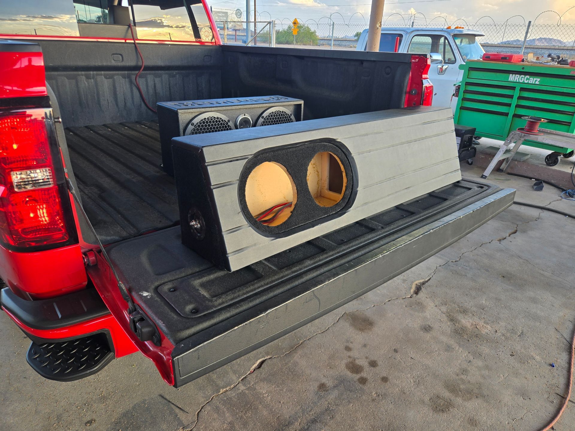 Custom gray speaker box with dual subwoofers in the bed of a red pickup truck